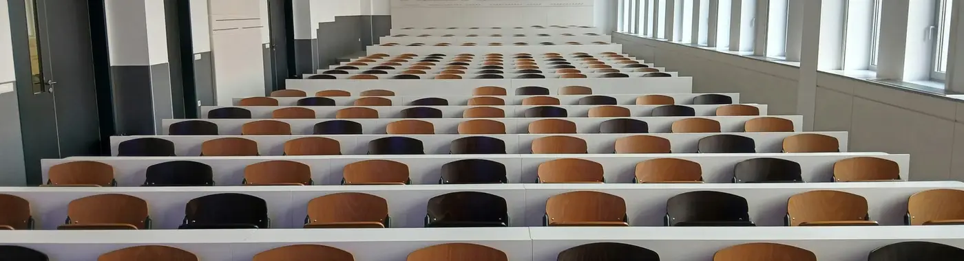 Ein leerer Hörsaal mit ansteigenden Sitzreihen in gedämpftem Licht.